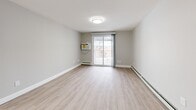 This 2-bedroom, 1-bathroom residence at 144 Dunbarton Rd in Manchester, NH offers a clean, modern layout across a single floor. The combined kitchen and living area serves as the heart of the home, featuring light wood-style flooring, neutral gray walls, and a sliding glass door that opens to a private balcony, filling the space with natural light. The kitchen is well-appointed with crisp white shaker cabinetry, a subway tile backsplash, stainless steel appliances including a refrigerator, dishwasher, and range, and a wall-mounted microwave — all complemented by light wood flooring for a cohesive look. The two bedrooms are carpeted in warm beige tones and painted in soft cream, each equipped with baseboard heating. The spacious primary bedroom benefits from dual windows that invite natural light and outdoor views. The second bedroom features a double-door closet. The full bathroom includes a soaking tub and shower combination with gold-toned fixtures set against clean white surroundings. A hallway connects the rooms efficiently, and the entry area includes an electrical panel. Baseboard heating is present throughout, ensuring comfort year-round.