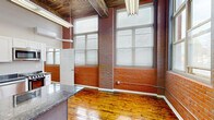 Located at 2074 Park St in Hartford, CT, this one-bedroom, one-bathroom loft-style unit masterfully blends industrial character with modern finishes. Rich hardwood floors run throughout, complemented by soaring ceilings adorned with rustic wood beam detailing that lend the space a dramatic, open feel. Exposed red brick walls punctuate the main living area and are framed by tall, large-pane windows fitted with blinds that flood the interior with generous natural light. The kitchen is a standout feature, outfitted with crisp white shaker cabinetry, dark granite countertops, a central granite-topped island, and a full suite of stainless steel appliances including a refrigerator, range, microwave, and dishwasher. The bedroom offers a comfortable, well-proportioned retreat beneath the same striking vaulted ceiling. The bathroom presents a clean, neutral aesthetic with large-format tile, a walk-in shower with marble mosaic accents, a wall-mounted vanity, and a drop ceiling with recessed lighting. The cohesive design throughout balances the raw, historic character of the building's architecture with thoughtful contemporary updates, resulting in a distinctive and functional living space.