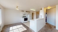 Located at 2055 NE Skyview Drive in Pullman, Washington, this single-floor unit offers a functional and well-lit layout designed for comfortable everyday living. The open-concept kitchen and living area form the heart of the space, where a peninsula counter separates the two zones while maintaining a sense of openness. The kitchen is equipped with white cabinetry offering ample storage, a electric range, a full-size refrigerator, and a double basin sink, all set atop easy-care vinyl flooring. The adjoining living area features plush carpet and is bathed in natural light from multiple windows, with a sliding glass door that opens to an outdoor view of the surrounding Pullman landscape. Multiple bedrooms provide comfortable retreats, each carpeted and featuring windows that allow natural light and views of the outdoors, along with baseboard heating for year-round comfort. The unit includes two bathrooms, each with white vanity cabinetry and clean, functional fixtures. Additional storage is accessible throughout, including a dedicated pantry or closet area visible near the kitchen. The overall palette of white walls and neutral tones gives the space a bright, clean character throughout.