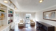 Located on Westheimer Road in Houston's vibrant 77098 corridor, this single-floor office space offers a well-appointed and functional environment suited for professional use. The layout features multiple dedicated work areas, including dark espresso-toned desks paired with ergonomic seating, providing ample room for individual or collaborative work. Rich hardwood flooring runs throughout, adding warmth and a polished aesthetic to the space.

A standout feature is the expansive built-in white shelving and cabinetry wall, which spans a full section of the office. It offers generous storage, display space, and integrated desk surfaces — ideal for an organized and productive workspace. Framed artwork adorns the walls, lending a refined, professional character to the interior.

Natural light floods the space through large sliding glass doors and floor-to-ceiling windows, which open onto an outdoor area with views of the surrounding greenery and courtyard below. A second set of glass-paned French doors provides additional access to the exterior. The textured ceilings with recessed and track lighting ensure the space remains well-lit throughout the day. A seating area with upholstered armchairs and a bistro table rounds out the space, offering a comfortable spot for meetings or informal conversations.