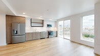 This well-designed one-bedroom, one-bathroom unit offers a thoughtfully efficient layout across a single floor. Light hardwood flooring flows throughout the entire space, lending a clean and cohesive aesthetic.

The open-concept kitchen and living area serves as the heart of the unit. The kitchen is outfitted with stainless steel appliances, including a gas range, over-the-range microwave, dishwasher, and French door refrigerator. Soft gray cabinetry with gold hardware pairs with white quartz countertops and a chevron-patterned tile backsplash for a contemporary look. Open black-framed shelving adds an industrial accent. A sliding glass door opens to a private balcony, filling the space with natural light and offering elevated city views.

The bedroom is a comfortable, well-lit retreat featuring a large picture window with additional city views and a spacious reach-in closet with built-in shelving and hanging rods. The room maintains the same clean white walls and hardwood flooring found throughout.

The bathroom features a long vanity with ample under-sink storage, gold hardware accents, a large mirror, and a full soaking tub-shower combination. The louvered utility closet near the entry provides additional in-unit storage and houses the washer and dryer.