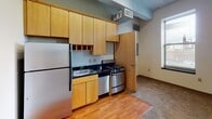 Located at 824 Hennepin Ave in the heart of Minneapolis, this single-floor unit reflects the character of an urban building with distinct industrial design elements. The exposed concrete beams and ceiling throughout the space lend a raw, loft-like aesthetic that is a hallmark of the building's architecture.

The kitchen is efficiently designed, featuring light wood cabinetry with ample upper and lower storage, dark countertops, a stainless steel range, a refrigerator, and a single-basin sink. A hardwood floor anchors the kitchen area, which transitions into carpet throughout the remainder of the unit. Natural light filters in through a window with views of the surrounding cityscape, adding a connection to the vibrant Hennepin Avenue neighborhood.

The living area is open and functional, with neutral-toned carpet, high ceilings defined by the exposed beam structure, and a built-in wood wardrobe providing convenient storage near the entry door. An additional carpeted room serves as a versatile space, illuminated by a window that brings in natural light.

The bathroom is compact and straightforward, featuring a wall-mounted sink, toilet, round mirror, and tile flooring. An electrical panel is conveniently accessible in the hallway just outside. Overall, the unit offers an urban, industrial ambiance well-suited to its central Minneapolis location.