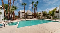Located at 10654 North 60th Avenue in Glendale, Arizona, this outdoor amenity area serves as a central gathering space within a multi-building residential community. The centerpiece is a generously sized swimming pool with crystal-clear turquoise water, complemented by an adjacent spa/hot tub that provides a dedicated space for relaxation. The pool deck is finished with a textured aggregate surface, offering ample room for lounge chairs and outdoor furniture throughout.

A covered pergola structure anchors one side of the pool area, providing shaded seating that is ideal for the Arizona sun. The surrounding landscape features tall, mature palm trees that lend a resort-like atmosphere, along with additional desert-friendly plantings and shrubs that line the perimeter. Iron fencing encloses the space, ensuring both security and clear sightlines to the surrounding buildings.

A poolside utility building with a tile roof houses support facilities and is accessible directly from the pool deck. The multi-story residential buildings surrounding the area are constructed in a Southwestern stucco style with tile rooflines, creating a cohesive architectural character throughout the community. Under the broad Arizona sky, this outdoor space delivers a bright, open, and inviting environment well-suited to year-round outdoor living.