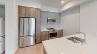 Located at 800 S Harvard Blvd in the Koreatown neighborhood of Los Angeles, this modern single-floor residence showcases a clean, contemporary design throughout. Light wood-tone flooring runs seamlessly across the living areas and bedrooms, complementing the bright white walls and recessed lighting that create a fresh, airy atmosphere.

The open-concept kitchen is a standout feature, equipped with stainless steel appliances including a gas range, built-in microwave, and a French door refrigerator. Flat-panel cabinetry in a two-tone wood and matte gray finish pairs with a white quartz countertop and a decorative hexagonal tile backsplash. A kitchen island with an integrated sink adds both function and a natural gathering point.

The living area is generously proportioned and filled with natural light from large sliding glass doors that open to a private balcony with outdoor views. The bedrooms are well-sized, with one featuring a large window overlooking the surrounding neighborhood and another offering a built-in sliding-door closet with shelving.

The bathrooms are appointed with neutral large-format floor tiles, wood-finish vanities topped with white quartz, round mirrors, and tiled tub-shower combinations. A smart thermostat is also present, adding a layer of modern convenience to this thoughtfully designed space.