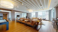 This expansive, single-floor lounge space showcases a refined contemporary design that seamlessly blends comfort with sophistication. The open-plan layout flows across multiple distinct zones, all united by warm hardwood flooring and a striking slatted white ceiling that adds architectural depth and texture throughout.

The main seating area features generously proportioned tan leather sofas with metal frames, complemented by a secondary lounge zone furnished with cream upholstered armchairs and wooden accent pieces, anchored by a vibrant blue-and-yellow area rug. Floor-to-ceiling windows line the perimeter, flooding the interior with abundant natural light and offering sweeping city skyline views.

A dedicated dining area accommodates a large round table surrounded by plush upholstered chairs with gold-toned frames, positioned beside full-height glazed windows that continue the connection to the urban panorama outside. Nearby, a stylish wet bar features a white stone countertop over rich, dark cabinetry with brass bar seating, all bathed in natural light from surrounding windows.

The space is further enhanced by designer drum pendant lighting, textured accent walls, wood-paneled details, and a billiards area visible in the floor plan. The overall ambiance is warm, polished, and thoughtfully curated for an elevated social experience.