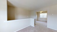 Located at Barrington Gardens, this single-floor residence offers a clean, straightforward layout designed for comfortable living. The interior is finished with wall-to-wall carpeting in a soft, neutral tone that runs throughout the space, creating a cohesive and understated aesthetic. Walls are painted in a warm beige, lending a calm, inviting atmosphere to the home.

A notable architectural detail is the white half-wall partition that divides areas of the living space, adding subtle definition without obstructing the open feel of the floor plan. The adjoining room is outfitted with a ceiling fan, providing both lighting and air circulation. A baseboard heating unit runs along the wall, ensuring year-round comfort.

Natural light enters through a window positioned along the far wall, brightening the interior and offering a view of the surrounding greenery outside. The overall design is practical and move-in ready, with a neutral palette that provides a versatile backdrop for a variety of interior styles. The single-level layout ensures easy accessibility throughout.
