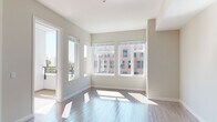 Located at 2155 Kettner Blvd in San Diego's vibrant Little Italy neighborhood, this single-floor unit offers a clean, modern aesthetic throughout. The open living area is bathed in natural light, courtesy of large, multi-pane windows that frame views of the surrounding urban streetscape, complemented by light wood-style flooring that extends across the main living spaces. A sliding door leads to a private balcony, further enhancing the connection to the outdoors.

The galley-style kitchen is well-appointed with white cabinetry, light countertops, a subway tile backsplash, and stainless steel appliances including a gas range, dishwasher, and built-in microwave. A louvered door adds a distinctive design touch at the kitchen entry. The bedrooms feature soft carpeting and windows with urban views, providing a quiet retreat from the main living areas.

The bathroom is finished with a modern floating vanity in a warm wood tone, white quartz countertops, a large mirror with overhead lighting, and a walk-in shower visible in the reflection. Neutral tile flooring ties the space together cleanly. Throughout the unit, a consistent palette of soft grays, whites, and warm neutrals creates a calm and cohesive atmosphere well-suited to contemporary urban living.
