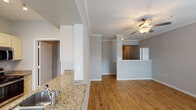 This single-story residence in Houston, TX offers a thoughtfully designed layout across two bedrooms and two full bathrooms. Wood-look flooring flows throughout the main living areas, complemented by crown molding and neutral gray walls that create a cohesive, modern aesthetic.

The kitchen is a functional galley-style space featuring granite countertops, a stainless steel double-basin sink, light wood cabinetry, stainless steel appliances including a refrigerator and electric range, and track lighting overhead. A peninsula counter opens toward the living and dining area, enhancing the sense of connectivity.

The living area benefits from multiple windows with blinds that invite natural light, a ceiling fan, and direct access to a private outdoor area via a glass door. A dedicated hallway leads to both bedrooms, with tile and wood-look flooring transitions marking distinct zones.

The primary bathroom features a long vanity with white cabinetry and leads to a walk-in closet with built-in shelving. The secondary bathroom includes a tiled tub-shower combination and overhead cabinetry. A separate in-unit laundry room accommodates a full-size washer and dryer. Crown molding is present throughout, adding a refined finish to each room.