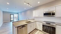 Located at 57 W Merritt Blvd in Fishkill, NY, this thoughtfully designed single-floor residence offers a clean, modern aesthetic throughout. The open-concept layout connects the living area seamlessly to the kitchen, creating a bright and functional living environment. Light wood-style flooring runs consistently throughout the main living spaces, lending warmth and continuity to the interior.

The kitchen is a standout feature, showcasing crisp white shaker-style cabinetry with ample upper and lower storage, sleek grey countertops, and a full suite of stainless steel appliances including a range, built-in microwave, dishwasher, and refrigerator. A peninsula with a undermount sink and track lighting above adds both utility and style, while an opening to the living area enhances the sense of openness.

The living space is generously proportioned, filled with natural light from multiple windows and French doors that lead directly to a private balcony, offering outdoor views of the surrounding neighborhood. Recessed lighting throughout adds a polished finish.

The bathrooms feature elegant marble-look tile flooring, modern vanities with white countertops, and chrome fixtures. Additional rooms offer versatile, neutrally finished spaces ready for a variety of uses. Overall, the unit presents a fresh, move-in-ready environment with contemporary finishes at every turn.