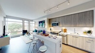 This thoughtfully designed single-floor residence offers a seamless blend of contemporary style and practical functionality. The open-concept layout connects the kitchen and living area, creating an expansive, light-filled space ideal for both everyday living and entertaining. Large floor-to-ceiling windows flood the living room with natural light and frame views of the surrounding cityscape, complemented by hardwood flooring and track lighting overhead.

The kitchen is a standout feature, equipped with a full suite of stainless steel appliances including a gas range, microwave, refrigerator, and dishwasher. Sleek wood-toned cabinetry extends to the ceiling for ample storage, while a white waterfall-edge island with bar seating serves as both a prep area and casual dining spot. White subway tile backsplash adds a clean, modern contrast.

The bedroom is a serene retreat, carpeted for comfort and featuring large windows that invite natural light and outdoor views. A gallery-style arrangement of framed artwork adds a curated, sophisticated touch.

The full bathroom is finished with large-format white tile flooring, a double-sink vanity with wood cabinetry, and a combination tub and shower with chrome fixtures.

Completing the residence is a dedicated in-unit laundry closet with a stacked washer and dryer and built-in shelving for added convenience.