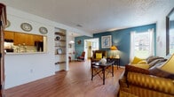 This single-floor residence offers a thoughtfully organized layout with a warm, lived-in character throughout. The living room serves as the heart of the home, featuring wood-look flooring, a textured ceiling, and a striking teal accent wall that adds a bold pop of color. Built-in open shelving provides both display and storage space, while natural light filters in through a window dressed with sheer curtains. The area flows openly toward a dining space and additional seating nook.

The kitchen includes warm wood cabinetry, light countertops, a double stainless steel sink with garbage disposal, and a dishwasher. A pass-through window connects the kitchen to an adjacent area, enhancing the open feel of the home.

A bright sunroom-style nook bathed in natural light from multiple windows offers a versatile sitting area with wood-look flooring and a pendant light fixture, ideal for reading or relaxing.

The bedroom is generously sized with plush carpeting, a ceiling fan, and a window allowing natural light. It includes ample closet space, with a dedicated walk-in closet housing built-in shelving.

The bathroom features wood-look flooring, a tub-shower combination, a single vanity with storage cabinetry, and clean, neutral finishes throughout.