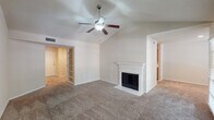 This single-story residence in Irving, Texas offers a well-organized layout with distinct living, kitchen, and bedroom areas. The main living room is a standout space, featuring vaulted ceilings that add a sense of openness and volume. A ceiling fan with integrated lighting enhances airflow and comfort, while a classically styled white-mantled fireplace serves as a natural focal point. Built-in shelving near the entryway provides functional storage, and soft neutral carpet runs throughout the living areas.

A secondary living or flex space connects via an open doorway and includes its own ceiling fan and French doors that invite natural light and views of the outdoors. The galley-style kitchen is outfitted with warm oak cabinetry, light countertops, a tile backsplash, and black appliances including a refrigerator, electric range, microwave, and dishwasher. Light wood-look flooring and track lighting complete the functional space, which also connects to a dedicated pantry or storage closet.

The bedrooms are carpeted and well-lit by large windows fitted with blinds, offering views of surrounding greenery. The bathroom features a full tub-shower combination with white tile surround, while a separate vanity area includes a wide mirror, wood cabinetry, and light flooring for a clean, practical finish.