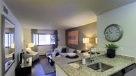 Located at 34 S Lexington Ave in White Plains, NY, this single-floor residence offers a well-designed open-concept layout that seamlessly blends the kitchen and living areas into one cohesive space. The kitchen is appointed with elegant granite countertops, a stainless steel sink, and a breakfast bar that serves as a natural divider between the cooking and living zones, making it ideal for both everyday use and entertaining.

The living area is warm and inviting, featuring dark hardwood-style flooring, a neutral color palette accented by a bold, darker feature wall, and tasteful décor including contemporary artwork. A large window allows natural light to fill the room, enhancing the open and airy feel of the space. A baseboard heating unit is positioned beneath the window, ensuring year-round comfort.

The overall ambiance is modern and sophisticated, with carefully curated lighting — including ambient table lamps — that create a cozy yet stylish atmosphere. The thoughtful layout maximizes the use of space while maintaining a clean, uncluttered aesthetic. This residence combines functional design with contemporary style, making it a comfortable and visually appealing home in the heart of White Plains.