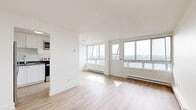 Located at 2969 Fairlea Cres in Ottawa's K1V neighbourhood, this 2-bedroom, 1-bathroom unit offers a clean, modern aesthetic throughout. Light wood laminate flooring runs continuously across all rooms, contributing to a bright and cohesive feel. The open living area is bathed in natural light from a large bank of windows that frame outdoor views, creating an airy atmosphere. Baseboard heating units line the walls throughout, providing efficient warmth. The kitchen is thoughtfully appointed with white shaker-style cabinetry, dark countertops, a double stainless steel sink, and stainless steel appliances including a refrigerator and stove. The layout connects the kitchen conveniently to the main living space. The primary bedroom is a well-proportioned room with a window overlooking the outdoors, allowing natural light to fill the space. The second bedroom is similarly bright with its own window and baseboard heating. The bathroom features classic white subway tile surrounding a full soaker tub and shower combination, complemented by clean white fixtures. Throughout the unit, the white walls and neutral finishes create a bright, move-in ready environment well-suited for comfortable everyday living.