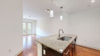 This well-appointed single-floor residence showcases a thoughtful open-concept layout that seamlessly connects the kitchen and living areas. The kitchen is a standout feature, centered around a large granite-topped island with an undermount stainless steel sink and elegant pendant lighting overhead. Dark espresso cabinetry provides ample storage and creates a striking contrast against the light granite surfaces, while stainless steel appliances — including a gas range, built-in microwave, and French door refrigerator — complete the modern culinary space. A neutral tile backsplash adds texture and refinement to the cooking area.

Rich, warm-toned hardwood flooring flows throughout the main living spaces and bedrooms, lending a sense of continuity and warmth. The living area benefits from soaring ceilings and direct access to an outdoor balcony through French doors, filling the space with abundant natural light and views of lush greenery. The bedrooms are generously proportioned, each with large windows that bring in natural light and offer pleasant outdoor views.

The bathroom is finished with coordinating dark cabinetry, a granite vanity top, subway tile surrounding the soaking tub and shower, and tile flooring — delivering a cohesive, polished aesthetic. Throughout the residence, clean white walls and consistent design elements create a bright, modern, and inviting atmosphere.