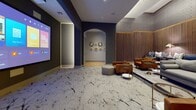 This sophisticated single-floor space is designed as a private screening room and social lounge, offering a refined blend of entertainment functionality and upscale interior design. The centerpiece of the room is a large-format VAVA projection screen mounted on a deep navy accent wall, flanked by integrated LED lighting that adds a dramatic, cinematic atmosphere. A ceiling-mounted projector ensures a sharp, immersive viewing experience.

The flooring throughout the screening area features a striking marble-patterned carpet with bold veining, lending an air of luxury underfoot. Adjacent to the screen wall, a generously sized lounge area is defined by rich, tufted cognac leather armchairs and plush gray sofas adorned with blue accent pillows. Warm-toned table lamps and sleek side tables complete this inviting social setting.

A standout design element is the full-height slatted wood accent wall, which introduces natural warmth and texture while providing excellent acoustic qualities suited to a screening environment. Decorative circular wall art punctuates the arched passageway connecting the screening zone to the entry corridor.

The entry corridor features light herringbone hardwood flooring, clean white walls, and a floating wood console with greenery, offering a welcoming transition into the space. The overall ambiance is moody, elegant, and thoughtfully curated for both entertainment and relaxed social gatherings.