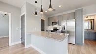 This thoughtfully designed 2-bedroom, 2-bathroom residence offers a clean, modern aesthetic throughout. The open-concept kitchen and living area serves as the heart of the home, anchored by a granite-topped island with an undermount sink and stylish pendant lighting. Gray shaker-style cabinetry, stainless steel appliances, and light hardwood flooring complete the kitchen's contemporary look. Large windows in the living area flood the space with natural light and provide views of the surrounding neighborhood. Both bedrooms feature plush carpeting, ceiling fans, and windows that bring in additional natural light. The primary bedroom includes a dedicated closet and an en-suite bathroom finished with granite countertops, gray cabinetry, and wood-look flooring. The second bathroom mirrors this refined aesthetic, offering a tiled tub-and-shower combination. Each bedroom is served by its own carpeted walk-in closet with built-in shelving and hanging rods for ample storage. A dedicated laundry area adds everyday convenience. Carpeted stairs connect to additional levels of the building. Neutral gray walls, white trim, and consistent finishes create a cohesive, move-in-ready atmosphere throughout the entire residence.