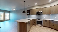 This contemporary single-floor residence is thoughtfully designed with a clean, modern aesthetic throughout. The open-concept layout connects the kitchen and living area seamlessly, creating a bright and functional living environment. Light hardwood-style flooring runs consistently throughout the space, contributing to a warm yet understated atmosphere.

The kitchen is a standout feature, equipped with a full suite of stainless steel appliances including a gas range, microwave, dishwasher, and refrigerator. Flat-front wood-tone cabinetry provides ample storage, complemented by light gray subway tile backsplash and crisp white countertops. A peninsula island with an undermount sink and stylish pendant lighting above adds both workspace and visual appeal. Track lighting illuminates the adjacent open living area, which is generously sized and receives natural light through large windows and double doors leading to a balcony.

The bathroom features a clean, minimalist design with a wood-tone vanity, white countertop, and a full soaking tub with shower. Neutral wall tones and consistent flooring carry the cohesive design language into this space as well. A dedicated closet with built-in shelving provides practical storage. Additional bedroom space offers a quiet, neutral retreat with ample room for furnishings. Overall, the space presents a polished, move-in-ready environment with modern finishes throughout.