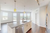 Located at 455 S Maple Ave in Falls Church, VA, this well-appointed 2-bedroom, 2-bathroom residence offers a thoughtfully designed open-concept layout. The combined kitchen and living area serves as the heart of the home, anchored by a central island with a granite countertop and an integrated sink. The kitchen is outfitted with stainless steel appliances, including a French door refrigerator, range, built-in microwave, and dishwasher, complemented by white cabinetry, a glass tile backsplash, and track lighting with stylish pendant fixtures overhead. Rich hardwood floors extend throughout the main living area, which is bathed in natural light from a wall of large windows offering open views of the surrounding landscape and city below. Both bedrooms feature plush carpeting and generous windows that continue the theme of bright, airy living. The primary bedroom includes an en-suite bath with a granite vanity, dark cabinetry, tile flooring, and a glass-enclosed shower. The second bathroom mirrors this refined aesthetic with a granite vanity and a tub-shower combination with subway tile surround. Additional conveniences include three closets, an in-unit laundry area, and a programmable thermostat, rounding out this polished and functional residence.