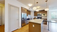 This well-appointed single-floor residence combines modern design with functional living across a thoughtfully laid-out floor plan. The open-concept kitchen serves as the heart of the home, showcasing warm wood-toned cabinetry that extends to the ceiling, granite countertops, and a large central island with pendant globe lighting overhead. Stainless steel appliances — including a French door refrigerator, electric range, and over-the-range microwave — complete the contemporary kitchen aesthetic. Light wood-style flooring flows throughout the main living areas, lending warmth and continuity to the space.

The living area is bright and airy, featuring multiple windows dressed with blinds and a sliding glass door that opens onto a private balcony with outdoor views of surrounding greenery. Ceiling fans are present throughout, adding comfort and airflow to each room.

The bedrooms are carpeted for comfort, each offering natural light through large windows and ceiling fans. At least one bedroom includes a dedicated closet with a hanging rod. The bathrooms are finished with granite-topped wood vanities, tiled tub-and-shower combinations with two-tone tile work, and wood-look flooring. A dedicated laundry area houses a full-size front-loading washer and dryer, adding everyday convenience to this well-designed home.