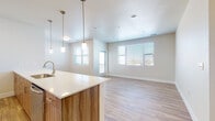 This single-floor residence showcases a clean, modern design characterized by neutral tones, light wood-style flooring, and an open layout that promotes a seamless flow between living spaces. The open-concept kitchen and living area serves as the heart of the unit, where a large island with a white quartz countertop and integrated sink takes center stage. Pendant lighting hangs above the island, complementing warm wood-toned lower cabinetry and upper cabinets that extend toward the ceiling. Stainless steel appliances, including a refrigerator, range, and microwave, complete the kitchen. A white subway tile backsplash adds a subtle textural detail. The adjoining living area benefits from multiple windows fitted with horizontal blinds, allowing ample natural light throughout the space. A glass-paneled door provides access to an exterior balcony. The bedrooms feature plush carpeting, ceiling fans with light fixtures, and generous closet space, including a set of double doors in one bedroom. Windows bring in additional natural light. The bathroom includes a wood-toned vanity with a white countertop, a soaking tub with tiled surround, and coordinating brushed nickel hardware throughout.