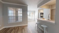 This single-floor residence offers a clean, modern aesthetic defined by neutral gray tones, white trim, and a thoughtful mix of flooring materials throughout. The entry and main living areas feature wood-look flooring that adds warmth and durability, while crown molding and textured ceilings lend a polished architectural character to the space. Large windows fitted with white horizontal blinds invite generous natural light into the living and dining areas, creating a bright and welcoming atmosphere.

The kitchen is well-equipped, featuring sleek cabinetry, stainless steel appliances including a range, microwave, and refrigerator, complemented by light countertops and a stylish tile backsplash. A breakfast bar with seating provides a casual dining option. An in-unit laundry area is conveniently accessible from within the home.

The bedrooms are finished with plush carpeting and equipped with ceiling fans for comfort. Each bedroom benefits from natural light through slatted windows, and at least one bedroom connects directly to a bathroom, enhancing functionality.

The bathrooms are well-appointed with wide vanities, white countertops, framed mirrors, contemporary lighting fixtures, and tub-shower combinations. Wood-look tile flooring ties the bathrooms seamlessly to the overall design language of the home, creating a cohesive and modern living environment throughout.