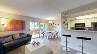 This efficiently designed 2-bedroom, 1-bathroom residence is laid out entirely on a single floor, making excellent use of its compact footprint. The open-concept living and dining area serves as the heart of the home, featuring light wood-tone flooring, a textured ceiling, and large sliding glass doors that flood the space with natural light and provide direct access to a covered private patio with a fenced yard. The living area offers comfortable space for lounging, while the adjacent dining area accommodates a full-sized table beneath a modern pendant light fixture.

The galley-style kitchen is well-appointed with white cabinetry, light quartz countertops, a double-basin sink, and black appliances including a range and refrigerator. A pass-through counter opening connects the kitchen to the main living area, enhancing the open feel of the space.

The primary bedroom provides a comfortable retreat with dark hardwood-style flooring and a textured ceiling. The second bedroom offers similar finishes and functionality. A dedicated closet provides additional storage.

The bathroom features a tiled shower-tub combination, a white vanity with a quartz countertop, and wood-tone flooring. Outside, the covered patio overlooks a fenced yard with mature trees visible beyond the perimeter, offering a pleasant outdoor extension of the living space.