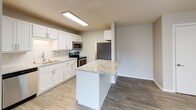 Located at 625 10th Ave S in Waite Park, Minnesota, this single-floor unit offers a well-organized layout designed for comfortable everyday living. The open-concept kitchen and living area form the heart of the space, connected by wood-look vinyl plank flooring that runs throughout the main living zones, lending a cohesive and clean aesthetic.

The kitchen is thoughtfully appointed with white shaker-style cabinetry, granite countertops, and a classic subway tile backsplash. A peninsula island with a matching granite surface provides additional prep space and a natural division between the kitchen and living area. Stainless steel appliances—including a refrigerator, electric range, over-the-range microwave, and dishwasher—complete the functional setup. Overhead fluorescent lighting ensures the kitchen remains well-lit.

The living area is open and versatile, with neutral wall tones and a textured ceiling. A wall-mounted air conditioning unit and baseboard heating offer year-round climate control. A sliding glass door or window allows natural light to filter into the space.

The bedrooms feature plush carpeting, baseboard heating, and natural light from windows with blinds. One bedroom includes a built-in closet with dual hanging rods. The bathroom is clean and straightforward, with a full tub-shower surround and standard fixtures throughout.