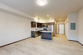 Located at 18705 67th Ave NE in Arlington, Washington, this thoughtfully designed unit offers a cohesive, single-level layout that maximizes its compact footprint. The open-concept main living area seamlessly combines the kitchen, dining, and living spaces, creating a bright and functional environment. The kitchen is a standout feature, outfitted with rich dark-stained cabinetry, a light-colored tile backsplash, stainless steel appliances including a refrigerator, range, microwave, and dishwasher, and a central island with a crisp white countertop that provides additional prep and dining space. Light-toned luxury vinyl plank flooring extends throughout the entire unit, lending a clean and modern aesthetic. The living area benefits from a window that frames views of the surrounding neighborhood and brings in natural light. The entrance hallway features a large sliding closet door, offering generous storage. The bathroom is finished with matching dark cabinetry, a stone-look countertop, and includes accessibility-friendly grab bars. An in-unit laundry area adds convenience. Recessed lighting and flush-mount fixtures provide consistent illumination throughout, contributing to the unit's fresh, move-in-ready feel.