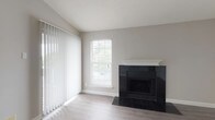 This single-floor residence offers a thoughtfully designed layout with a clean, contemporary aesthetic throughout. The living room serves as a central gathering space, highlighted by a striking black-tiled fireplace with a white mantle that anchors the room. Light-toned luxury vinyl plank flooring extends across the main living area, complemented by neutral gray walls and a textured ceiling. Large vertical blinds and a double-hung window allow natural light to filter in, creating a bright, open atmosphere.

The kitchen is well-appointed with dark wood cabinetry on the lower cabinets paired with crisp white upper cabinets, a blue tile backsplash, and white quartz countertops. A peninsula provides additional prep and seating space. Stainless steel appliances, including a refrigerator, range, microwave, and dishwasher, complete the functional setup. Light wood-look flooring ties the kitchen to the adjoining living area seamlessly.

The bedroom features plush wall-to-wall carpet, neutral walls, and a window with blinds that admits natural light. The bathroom includes a full soaking tub with a decorative striped tile surround, dark tile flooring, and chrome fixtures, offering a polished, modern finish.
