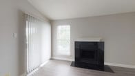 This single-floor residence offers a thoughtfully designed layout with a clean, contemporary aesthetic throughout. The living room serves as a central gathering space, highlighted by a striking black-tiled fireplace with a white mantle that anchors the room. Light-toned luxury vinyl plank flooring extends across the main living area, complemented by neutral gray walls and a textured ceiling. Large vertical blinds and a double-hung window allow natural light to filter in, creating a bright, open atmosphere.

The kitchen is well-appointed with dark wood cabinetry on the lower cabinets paired with crisp white upper cabinets, a blue tile backsplash, and white quartz countertops. A peninsula provides additional prep and seating space. Stainless steel appliances, including a refrigerator, range, microwave, and dishwasher, complete the functional setup. Light wood-look flooring ties the kitchen to the adjoining living area seamlessly.

The bedroom features plush wall-to-wall carpet, neutral walls, and a window with blinds that admits natural light. The bathroom includes a full soaking tub with a decorative striped tile surround, dark tile flooring, and chrome fixtures, offering a polished, modern finish.