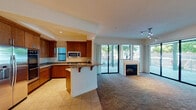 This single-floor residence offers a thoughtfully designed open-concept layout that seamlessly connects the kitchen, dining, and living areas. The living room is a welcoming focal point, anchored by a fireplace and bathed in natural light streaming through expansive floor-to-ceiling sliding glass doors that open to a spacious covered patio. The patio, framed by bold architectural columns and metal railings, overlooks a landscaped outdoor setting with mature trees.

The kitchen is well-equipped with rich wood cabinetry, granite countertops, stainless steel appliances including a built-in microwave and gas cooktop, and a breakfast bar for casual dining. Tile flooring runs throughout the kitchen and dining areas, transitioning to plush carpeting in the living and bedroom spaces.

The primary bathroom is a refined retreat featuring a soaking tub with stone tile surround, a separate glass-enclosed walk-in shower with a rain showerhead, a single vanity with wood cabinetry, and recessed lighting. A second full bathroom mirrors similar finishes with a tub-shower combination and stone tile accents. Bedrooms feature ceiling fans, ample closet space, and wood-look flooring, while the primary suite benefits from an expansive walk-in closet with full wire shelving systems.