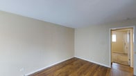 This single-floor space presents a straightforward and functional layout designed to accommodate a variety of uses. The interior is characterized by rich, dark hardwood flooring that runs throughout, adding warmth and a classic aesthetic to the space. The walls are finished in a soft, neutral beige tone that creates a calm and inviting atmosphere, complementing the natural tones of the flooring. Crisp white baseboards provide a clean visual transition between the walls and the floor, lending a polished, well-maintained appearance. The white ceiling is smooth and bright, contributing to an open and airy feel within the room. Electrical outlets are conveniently positioned along the walls, offering practical utility throughout the space. The minimalist, unfurnished state of the interior allows for a clear view of its proportions and finishes, making it easy to envision a range of configurations and uses. Overall, the space offers a clean, neutral canvas with quality finishes that provide a solid foundation for any intended purpose.