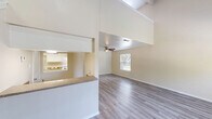 Located at 1201 S Johnson St in Alvin, TX, this two-story home offers a well-organized layout spread across two floors. The main floor houses the primary living spaces, including a bright and open living room highlighted by soaring vaulted ceilings, a ceiling fan, and a window that invites natural light while offering a view of the outdoors. Light gray wood-style flooring runs throughout, adding a clean and modern aesthetic. A staircase with carpeted treads and a stylish pendant light leads to the upper level. The galley-style kitchen is efficiently designed with white cabinetry, stone-look countertops, a stainless steel sink, white appliances, and overhead lighting — offering ample storage and workspace. The bathroom features a full tub-shower combo, toilet, and a classic raised-panel door detail. Upstairs, the upper level provides a more intimate space characterized by sloped ceilings that follow the roofline, a large window with blinds framing an outdoor garden view, a built-in ledge, and a ceiling fan — making it a versatile area suited for a bedroom, office, or retreat. Throughout the home, warm neutral wall tones and consistent flooring create a cohesive and inviting atmosphere.