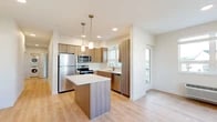 Located at 10999 SE 37th Ave in Portland, Oregon, this single-floor home offers five bedrooms and two full bathrooms within a thoughtfully designed layout. The open-concept kitchen and living area serves as the heart of the home, featuring warm wood-tone cabinetry, a central island with a white quartz-style countertop, stainless steel appliances including a refrigerator, range, microwave, and dishwasher, and stylish pendant lighting overhead. Light wood-tone flooring extends through the kitchen and living areas, creating a bright, cohesive feel. The living space is generously proportioned and flows naturally from the kitchen, providing a versatile area for everyday use. Two hallways connect the various parts of the home efficiently. The five bedrooms are finished with neutral-toned carpet and warm wall colors, offering a comfortable, quiet retreat. Several bedrooms feature windows with views of the surrounding neighborhood, allowing natural light to fill the rooms. Closet space is included in the bedrooms for added practicality. Both bathrooms are finished consistently with wood-tone vanities, white countertops, light wood-look flooring, and full tub-shower combinations with chrome fixtures, maintaining the home's clean, modern aesthetic throughout.