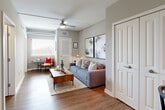 This thoughtfully designed 1-bedroom, 1-bathroom unit maximizes every square foot with a modern, functional layout across a single floor. The living room serves as the heart of the unit, featuring warm hardwood-style flooring, soft neutral gray walls, a ceiling fan, and a large window that invites natural light to fill the space. Framed abstract artwork anchors the main wall, complementing the contemporary aesthetic throughout.

The galley-style kitchen is efficiently organized with light wood cabinetry, dark quartz countertops, a subway tile backsplash, and a full suite of stainless steel appliances, including a refrigerator, microwave, and dishwasher. A deep undermount sink adds a clean, functional touch.

The bedroom is a cozy, serene retreat featuring hardwood-style flooring, soft neutral tones, and a distinctive sliding barn door in gray. A ceiling fan keeps the space comfortable year-round.

The bathroom is finished with clean, modern details including a frameless glass walk-in shower fully tiled in white subway tile, a wood-toned vanity with dark countertop, and hardwood-style flooring. Every room reflects a consistent, contemporary design language that balances style and practicality throughout this efficiently planned unit.