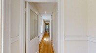 Located at 300 E 30th St in Baltimore's vibrant Charles Village neighborhood, this three-bedroom, one-bathroom home offers a well-organized single-floor layout with over 1,200 square feet of living space. A welcoming entrance leads into a bright living room highlighted by a striking white-painted brick fireplace with decorative blue tile accents, gleaming hardwood floors, and dual windows that fill the space with natural light. A long, light-filled central hallway — featuring recessed lighting, hardwood flooring, and side windows — connects the main living areas to the bedrooms, creating a clean and functional flow throughout the home. The updated kitchen stands out with slate-gray cabinetry, brass hardware, quartz countertops, subway tile backsplash, and elegant marble-look tile flooring. The three bedrooms are bright and spacious, with warm hardwood floors, natural light from windows, and built-in closets in select rooms. The primary bedroom is generously sized, offering ample room for furnishings. The bathroom is tastefully renovated with marble-look tile flooring, a soaking tub with tiled surround, a modern vanity, and brushed nickel fixtures. Throughout the home, crisp white walls and classic trim work lend a clean, timeless aesthetic.