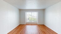 Located at 6240 Ridgecrest Rd in Dallas, Texas, this single-story unit features a consistent, clean aesthetic throughout, with warm-toned hardwood-style flooring that flows seamlessly across all living areas, bedrooms, and bathrooms. The neutral white walls and textured ceilings provide a bright, open canvas in each room.

The living areas are well-proportioned, with large windows that invite natural light and offer views of surrounding greenery. Multiple bedrooms are present, each equipped with ceiling fans and windows fitted with blinds. The bedrooms benefit from generous walk-in closets, one of which includes a built-in shelving unit for added organization, while another features dual hanging rods and additional shelving.

The kitchen is outfitted with warm wood cabinetry, speckled laminate countertops, a double stainless steel sink, and a white dishwasher, with a window providing natural light. The bathrooms feature white tile surrounds on the tub-shower combinations, speckled vanity countertops with white cabinetry, large mirrors, and overhead lighting, maintaining a clean and functional design throughout.