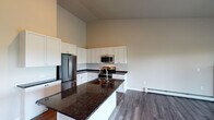 This single-floor unit is defined by clean, modern finishes and a thoughtfully designed open layout. The kitchen serves as the centerpiece, showcasing white shaker-style cabinetry extending to dramatically vaulted ceilings, dark granite countertops, and a full suite of stainless steel appliances including a refrigerator, range, microwave, and dishwasher. A central island with an undermount sink and matching granite provides additional workspace and casual dining potential. Hardwood-style plank flooring runs throughout the unit, adding warmth and continuity.

The living area is generously proportioned, benefiting from the soaring ceiling height and sliding glass doors that open onto a deck overlooking an open landscape. The bedrooms are well-sized, each featuring windows with outdoor views, ceiling fans, and baseboard heating. The primary bathroom is outfitted with a dual-sink vanity, dark granite countertops, white shaker cabinetry, a tall linen tower, and large mirrors. A dedicated laundry area includes a full-size GE front-load washer and dryer alongside wire shelving for storage. The unit also includes a fireplace visible from the main living space.