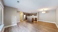 This thoughtfully designed one-bedroom, one-bathroom unit offers a functional and modern living experience across a single floor. The open-concept layout seamlessly connects the kitchen and living area, creating a spacious, airy feel ideal for both everyday living and entertaining. The kitchen is a standout feature, equipped with rich medium-toned wood cabinetry, crisp white countertops, a full suite of stainless steel appliances including a refrigerator, range, microwave, and dishwasher, and a center island that provides additional prep space and seating. Warm wood-look luxury vinyl plank flooring runs throughout the main living areas, adding a clean, contemporary aesthetic. Neutral taupe-toned walls complement the finishes and provide a versatile backdrop throughout the unit. The bedroom is a comfortable size, featuring plush carpeting, a large window that allows in natural light, and access to a dedicated closet. The full bathroom is clean and functional, appointed with a tub-shower combination with white tile surround and matching fixtures. A separate hallway connects the primary spaces, adding a sense of defined flow. Natural light from multiple windows throughout the unit enhances its open and welcoming atmosphere.