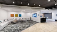Located at 13682 Fraser Hwy in Surrey, BC, this thoughtfully designed amenity space spans a generous single floor, offering a dynamic blend of social, recreational, and lounge areas. The interior showcases a contemporary aesthetic characterized by crisp white walls, dark exposed ceilings with industrial-style ductwork and black piping, and a sophisticated combination of light hardwood flooring and patterned carpet tiles throughout.

The welcoming lounge area features plush modular grey sofas accented with colorful cushions, complemented by curated artwork and large-format display screens mounted on the walls. A reception-style counter anchors the space, adding a polished, professional touch. Adjacent seating nooks with additional sofas and accent tables provide inviting spaces for casual gatherings.

The recreational area is a standout highlight, equipped with a billiards table, a ping pong table, and a foosball table, all set within an open, light-filled zone with floor-to-ceiling windows offering outdoor views. A glass-walled room provides a dedicated, semi-private area for table tennis. The space also includes a private room, storage closet, and additional flex areas. Throughout, recessed and track lighting ensures a bright, welcoming atmosphere suited to both relaxation and active recreation.