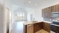 Located at 12890 S Black Bob Rd in Olathe, Kansas, this single-floor, 3-bedroom, 3-bathroom unit showcases a clean, contemporary design with consistent modern finishes throughout. The open-concept kitchen and living area is anchored by soaring vaulted ceilings and large floor-to-ceiling windows that flood the space with natural light and provide views of the surrounding community. The kitchen features rich dark wood cabinetry, a stone-topped peninsula island with an undermount sink, a tile backsplash, and stainless steel appliances including a refrigerator, microwave, and dishwasher. Light hardwood flooring flows throughout the main living areas, while the bedrooms are finished with plush carpet. Each bedroom offers ceiling fans and well-proportioned layouts, with the primary bedroom benefiting from a generous walk-in closet outfitted with built-in shelving and hanging rods. The primary bathroom includes a dual-sink vanity with stone countertops, dark wood cabinetry, and a glass-enclosed tiled walk-in shower. An in-unit laundry closet houses a full-size washer and dryer. A private outdoor balcony is accessible from the living area, completing this well-appointed space.