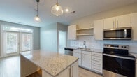 Located at 508 W High St in Lawrenceburg, Indiana, this single-floor residence offers a thoughtfully designed layout with contemporary finishes throughout. The open-concept kitchen serves as the heart of the space, showcasing light wood cabinetry with sleek hardware, granite countertops, and a classic white subway tile backsplash. A central island with matching granite provides additional workspace and casual seating, while pendant lighting adds a warm, stylish touch overhead. The kitchen is fully equipped with a complete suite of stainless steel appliances, including a refrigerator, range, over-the-range microwave, and dishwasher. Light wood-tone flooring runs throughout the main living and kitchen areas, creating a clean, cohesive aesthetic. The bedrooms are carpeted for comfort and benefit from natural light through windows fitted with horizontal blinds; one bedroom includes a ceiling fan. The primary bathroom is well-appointed with a double-sink vanity topped with granite, framed mirrors, a glass-enclosed shower, and wood-look flooring. A secondary bathroom features a tub-shower combination with brushed nickel fixtures. The overall design is clean and modern, with a neutral color palette that creates a bright and inviting atmosphere throughout.