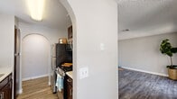 This single-story residence showcases a thoughtful layout with a blend of functional design and architectural charm. A defining feature throughout the home is the elegant arched entryways, which lend a distinctive character to the interior and create seamless transitions between spaces.

The galley-style kitchen is well-appointed with rich dark cabinetry, stainless steel appliances including a full-size refrigerator and gas range, and a layout that maximizes efficiency. Natural light filters in through a window at the far end, brightening the space and offering a pleasant view into the adjacent living area.

The living and bedroom areas feature wood-look plank flooring in a cool gray tone, complemented by neutral walls and textured ceilings throughout. The bedrooms are generously sized, with one featuring a walk-in closet and a window dressed with blinds that allows for natural light.

The bathroom is a standout space, offering a floating dual vanity with dark cabinetry and a white countertop, a large mirror, and well-placed vanity lighting. A soaking tub adds a touch of comfort and relaxation, while wood-look flooring continues the cohesive design aesthetic found throughout the home. The overall ambiance is clean, neutral, and move-in ready.