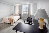 Located on the 9th floor of 180 King Street in downtown London, Ontario, this efficiently designed studio unit makes excellent use of its compact footprint. The main living area features light grey laminate flooring, neutral white walls, and a textured ceiling, creating a clean and bright atmosphere throughout. Large windows dressed with cream curtains invite abundant natural light while offering elevated views of the surrounding cityscape and horizon.

The sleeping area accommodates a full-sized bed and is positioned to take advantage of the generous window light. Adjacent to the sleeping space is a functional work area, providing room for a desk and chair — ideal for remote work or study. The kitchenette is neatly integrated into the space, outfitted with white shaker-style cabinetry, a subway tile backsplash, a stainless steel refrigerator, a gas range, and a single-basin sink — delivering essential cooking amenities in a thoughtfully arranged layout.

The bathroom features a tub-shower combination with striking large-format marble-effect tile surrounds in grey and white tones, lending a polished and upscale feel to the space. Throughout the unit, the consistent use of light tones and natural materials contributes to an open, airy ambiance despite the studio's compact scale. This unit is well-suited for a single occupant seeking a self-contained, conveniently located residence in the heart of London.