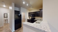 This single-floor residence offers a thoughtfully designed layout that balances comfort and functionality. The kitchen serves as a standout feature, showcasing rich dark cabinetry, light granite countertops, and a full suite of black appliances including an electric range, microwave, dishwasher, and refrigerator. Track lighting illuminates the space, while wood-look flooring adds warmth. A peninsula counter provides additional prep space and casual seating. An adjacent walk-in pantry offers generous storage.

The living area is open and airy, benefiting from vaulted ceilings and a sliding glass door that invites natural light and provides access to an outdoor balcony. Soft carpet flooring extends throughout the living and bedroom spaces.

The primary bedroom features a tray ceiling with an elegant chandelier, a bright window, and direct access to a spacious walk-in closet outfitted with multi-tier wire shelving. A secondary bedroom also includes its own walk-in closet with ample shelving and hanging space.

Two bathrooms serve the residence. One features a dark vanity with a granite countertop and lighted mirror, while the other is a compact half-bath with a pedestal sink. Both bathrooms include wood-look flooring that complements the overall design aesthetic of the home.