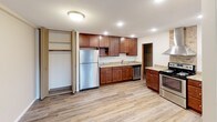 This single-floor space is thoughtfully laid out with an open-concept design that connects the kitchen and living areas seamlessly. The kitchen is well-appointed with rich, warm-toned cabinetry, granite-style countertops, and a full suite of stainless steel appliances, including a refrigerator, dishwasher, and electric range topped by a stainless steel wall-mounted range hood. A stone tile backsplash adds a decorative accent behind the range, while a peninsula with a granite countertop provides additional workspace and visual separation from the adjacent living area. Recessed lighting brightens the kitchen throughout.

The living area is generously sized, featuring large windows with wood-trimmed frames that bring in abundant natural light and outdoor views. A door provides direct exterior access. The bedrooms are comfortable and well-lit, each equipped with ceiling fans and windows. One bedroom offers notable storage with two sets of full-height bifold closet doors. The bathrooms are clean and functional — one features a pedestal sink, full tub-shower combination, and classic tile flooring, while the second includes a vanity with a wide mirror and wall-mounted cabinetry. Gray wood-look flooring runs consistently throughout the entire space, contributing to a cohesive, modern aesthetic.