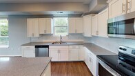 This single-floor unit located along County Road D E in Maplewood, Minnesota, offers a thoughtfully designed layout with modern finishes throughout. The expansive living area is finished with rich hardwood-style flooring and bathed in natural light from multiple large windows, with sliding glass doors providing direct access to a private balcony overlooking lush greenery. The open, airy feel is enhanced by soft blue-gray wall tones and clean white trim.

The kitchen is a functional centerpiece, featuring crisp white shaker-style cabinetry, light gray stone countertops, a classic subway tile backsplash, and a full suite of stainless steel appliances including a range, microwave, dishwasher, and refrigerator. A central island provides additional prep and storage space.

The bathrooms are finished with gray walls, wood-style flooring, and stone-topped vanities with white cabinetry. One bathroom includes a walk-in shower, while the other features a soaking tub with shower combination. A generously sized walk-in closet offers extensive wire shelving and hanging storage. A dedicated laundry room houses a full-size front-loading washer and dryer. Bedrooms feature plush carpeting and natural views.