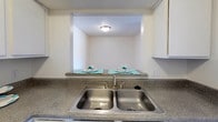 Located at 4330 N Grandview Ave in Odessa, TX, this single-floor unit offers a practical and comfortable layout designed for easy living. The living room serves as the heart of the space, featuring plush carpeting, a large window with vertical blinds that invites natural light, and a striking wood-paneled fireplace with a tile hearth and mantel — a standout focal point that adds warmth and character to the room. An adjacent carpeted bedroom provides a quiet retreat with a generous walk-in closet and a window overlooking the exterior. A second carpeted room offers versatile space with bright, neutral walls and a textured ceiling. The kitchen is efficiently designed with white cabinetry, granite-look countertops, a double stainless steel sink, and an electric range with overhead ventilation. A convenient pass-through counter connects the kitchen to a casual dining nook, making entertaining simple. The bathroom features wood-look flooring, a vanity with matching countertops, and a full shower-tub combination. Throughout the unit, textured ceilings and neutral tones create a clean, cohesive aesthetic. The entryway transitions from wood-look flooring to carpet, setting a welcoming tone from the moment you arrive.