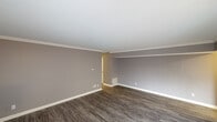This single-floor residence offers a well-organized layout finished in a consistent neutral gray palette with crisp white trim and textured ceilings throughout. The main living area is generously proportioned, featuring durable dark wood-look vinyl plank flooring, crown molding, and a built-in wall ledge that adds a subtle architectural detail. Natural light flows in through a large sliding glass door, enhancing the open feel of the space. An adjacent area with lighter vinyl plank flooring provides additional flexible living space.

The galley-style kitchen is efficiently designed, featuring warm medium-toned wood cabinetry with arched upper door details, dark granite-look countertops, a double stainless steel sink, and black appliances including a range and refrigerator. Light tile-look flooring and a subway tile backsplash complete the kitchen's clean aesthetic.

The two bedrooms are carpeted with plush tan carpet, each painted in the same calming gray tones. One bedroom includes a ceiling fan with light fixture and a window with natural views, while the other features a sliding closet door revealing a rod-and-shelf storage system. The full bathroom includes a tiled tub-shower combination with a window providing natural light and ventilation.